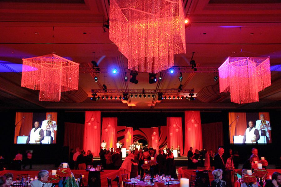 Red-themed banquet hall with chandeliers and screens.