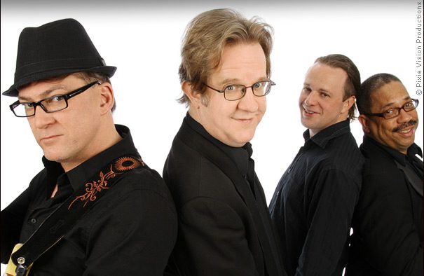 Four men standing back to back, smiling.