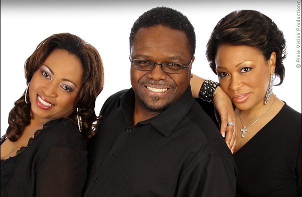 Three people smiling in black outfits.